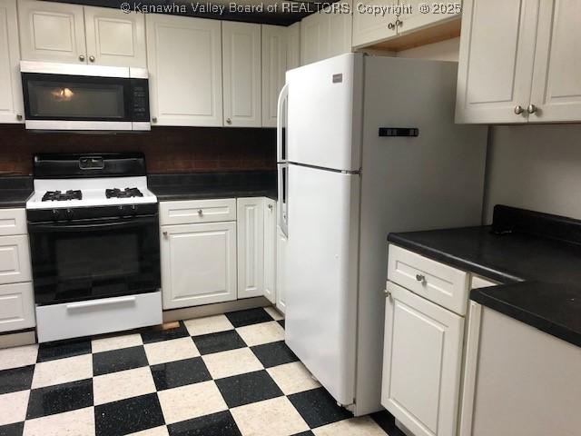 kitchen with white appliances, light floors, dark countertops, and white cabinets