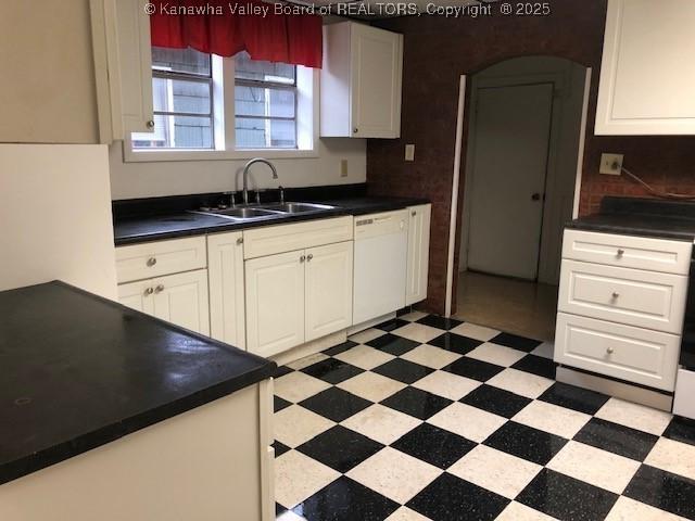 kitchen featuring a sink, dark countertops, light floors, and dishwasher