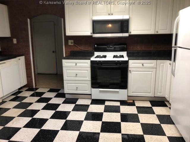 kitchen with gas stove, light floors, freestanding refrigerator, white cabinets, and stainless steel microwave