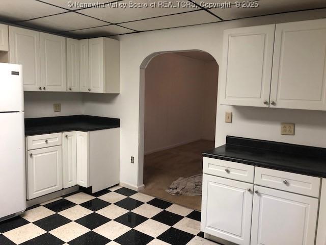 kitchen featuring dark countertops, light floors, arched walkways, and freestanding refrigerator