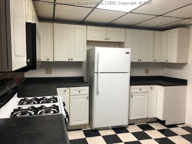 kitchen with dark countertops, light floors, white appliances, and white cabinets