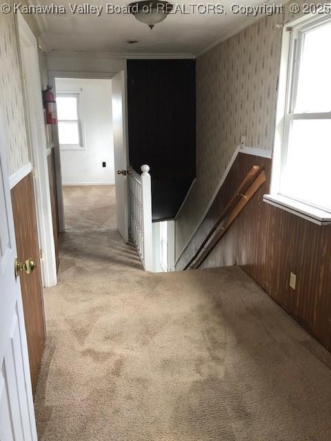 corridor with an upstairs landing, light carpet, crown molding, and wallpapered walls