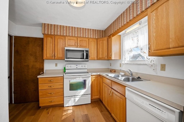 kitchen with white appliances, light countertops, light wood-type flooring, and a sink