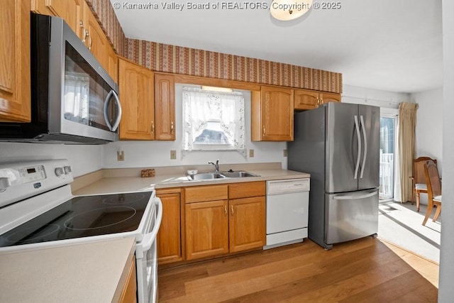 kitchen featuring light countertops, brown cabinets, appliances with stainless steel finishes, light wood-style floors, and a sink