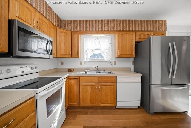 kitchen featuring light wood-style flooring, appliances with stainless steel finishes, light countertops, and a sink