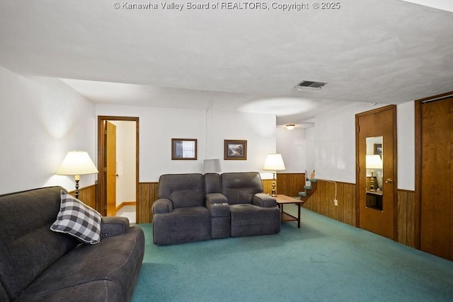 carpeted living area with wooden walls, visible vents, and a wainscoted wall