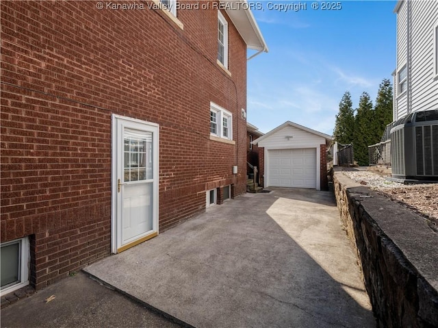 view of side of property featuring central air condition unit, an outbuilding, driveway, a detached garage, and brick siding