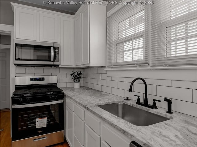 kitchen with a sink, backsplash, appliances with stainless steel finishes, and white cabinets