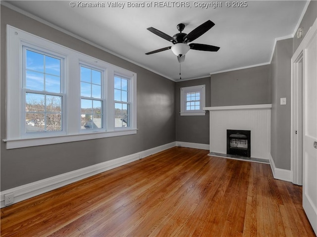 unfurnished living room with wood finished floors, a fireplace, crown molding, baseboards, and ceiling fan