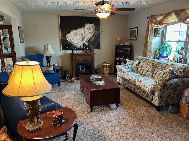 living room featuring carpet floors, a textured ceiling, a glass covered fireplace, and a ceiling fan