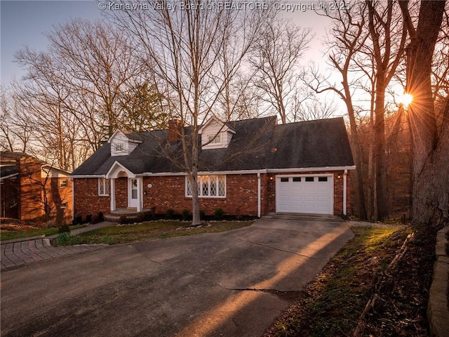 new england style home featuring brick siding, driveway, a chimney, and a garage