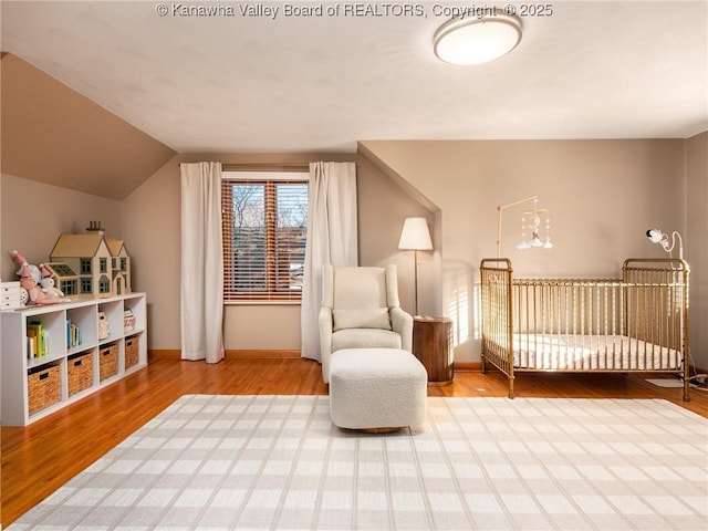 bedroom with vaulted ceiling, a nursery area, wood finished floors, and baseboards