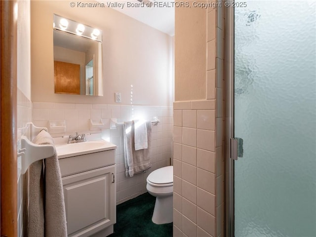 full bath with vanity, a shower stall, wainscoting, tile walls, and toilet