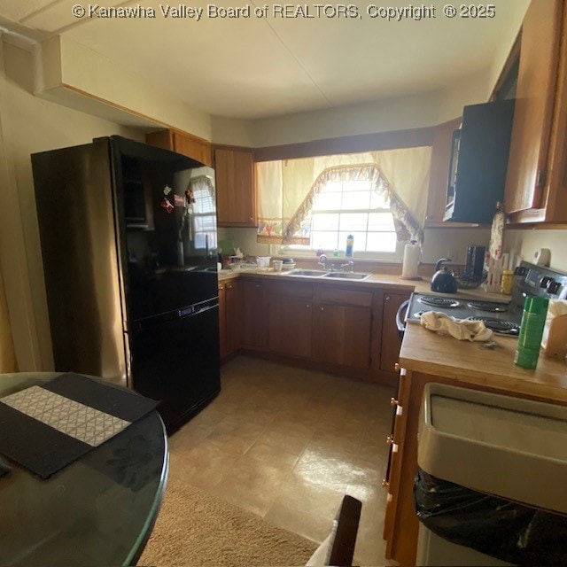 kitchen with brown cabinetry, stainless steel electric range, freestanding refrigerator, and a sink