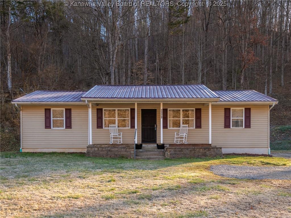 ranch-style house with a forest view, metal roof, a porch, and a front yard