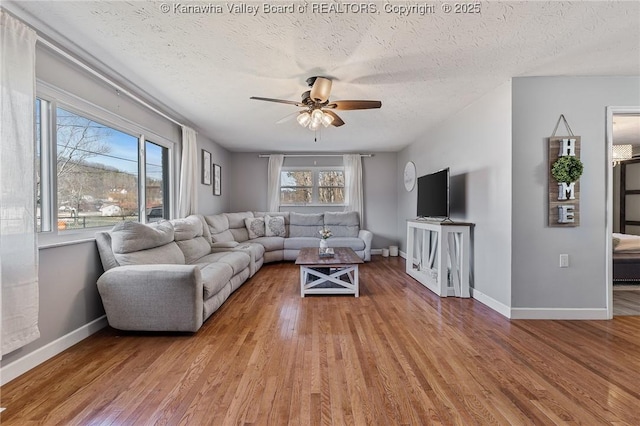 living area featuring light wood finished floors, ceiling fan, a textured ceiling, and baseboards