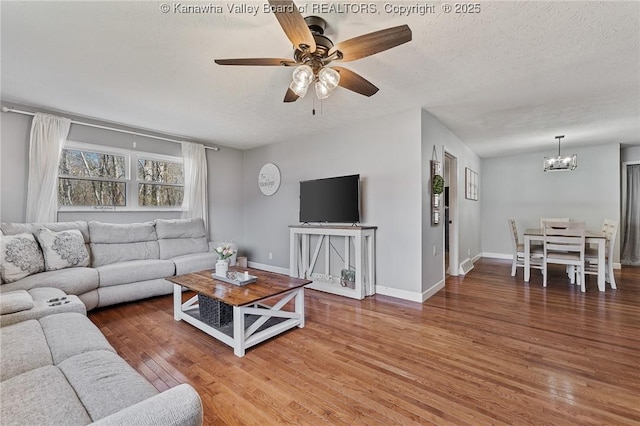 living area with ceiling fan with notable chandelier, a textured ceiling, wood finished floors, baseboards, and vaulted ceiling