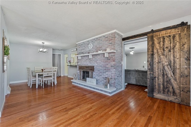 unfurnished living room with a brick fireplace, baseboards, a barn door, hardwood / wood-style floors, and a textured ceiling