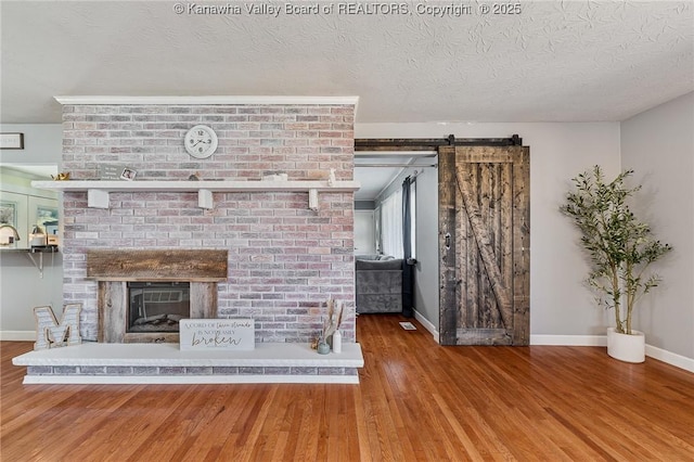 unfurnished living room featuring a textured ceiling, wood finished floors, a barn door, a fireplace, and baseboards