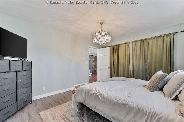 bedroom with wood finished floors, visible vents, a chandelier, and baseboards