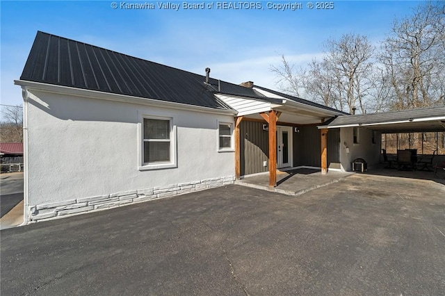 rear view of house featuring metal roof, a carport, and stucco siding