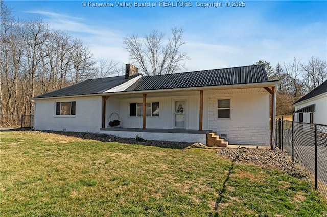 rear view of house with a chimney, a lawn, metal roof, and fence