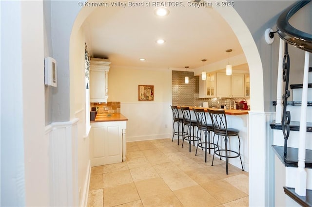 kitchen featuring backsplash, a kitchen bar, ornamental molding, recessed lighting, and arched walkways