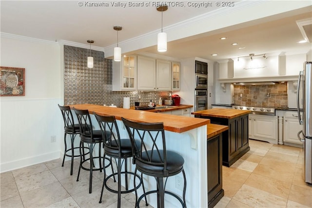 kitchen with appliances with stainless steel finishes, a peninsula, butcher block counters, crown molding, and glass insert cabinets