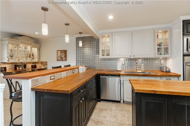 kitchen featuring dark cabinetry, a sink, stainless steel appliances, a kitchen breakfast bar, and butcher block counters