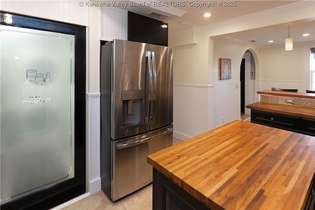 kitchen featuring a wainscoted wall, stainless steel fridge, arched walkways, and butcher block counters