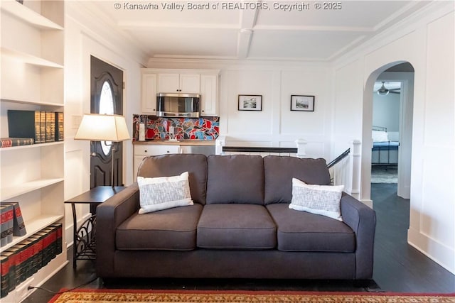 living room with arched walkways, a decorative wall, coffered ceiling, and built in features