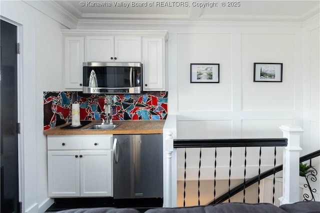 kitchen featuring ornamental molding, decorative backsplash, appliances with stainless steel finishes, white cabinetry, and a sink