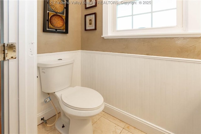 bathroom with tile patterned floors, toilet, and a wainscoted wall