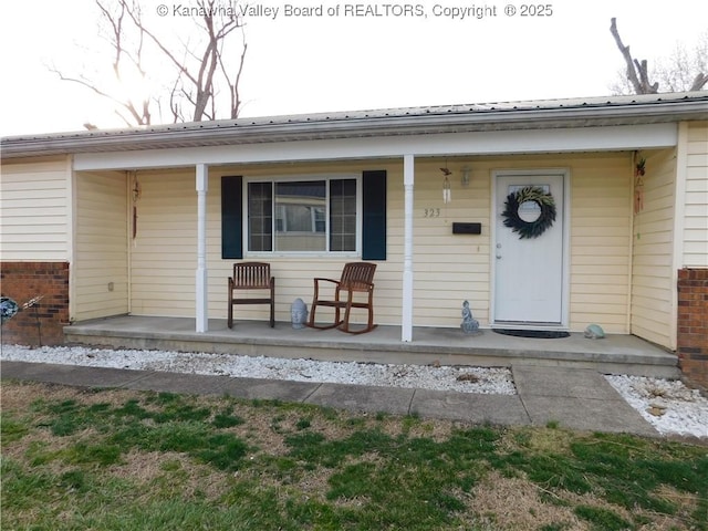 doorway to property featuring brick siding, a porch, and metal roof