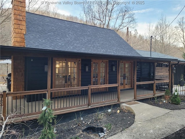 exterior space with a porch, french doors, a shingled roof, and a chimney