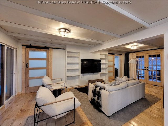 living area with hardwood / wood-style floors, a barn door, beamed ceiling, and french doors