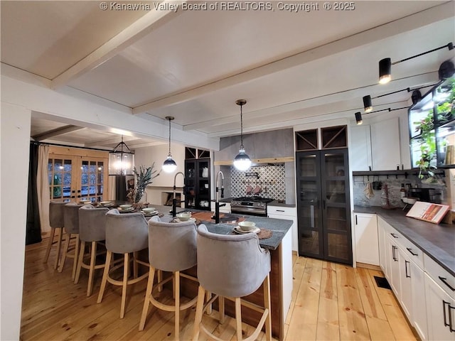 kitchen with dark countertops, tasteful backsplash, beamed ceiling, light wood-type flooring, and french doors