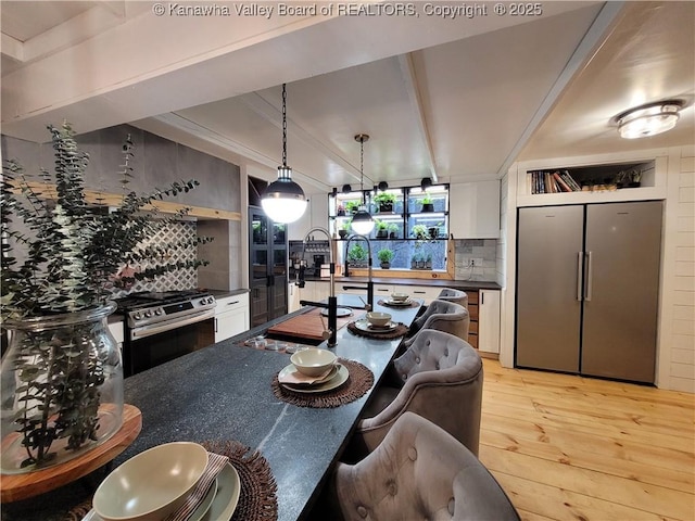 kitchen featuring light wood-type flooring, beamed ceiling, tasteful backsplash, dark countertops, and stainless steel appliances