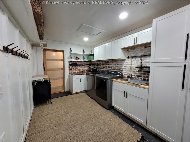 kitchen with washing machine and clothes dryer, open shelves, decorative backsplash, white cabinetry, and a sink