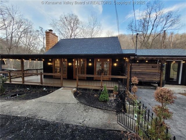 view of front of property with a porch, a shingled roof, a chimney, french doors, and aphalt driveway