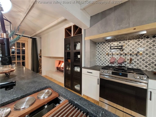 kitchen with range hood, stainless steel range with gas cooktop, white cabinetry, dark countertops, and tasteful backsplash