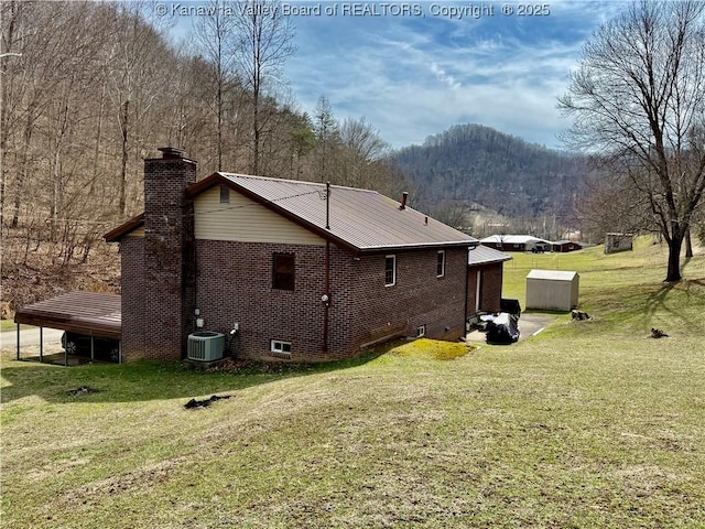 view of property exterior with brick siding, cooling unit, a chimney, metal roof, and a yard