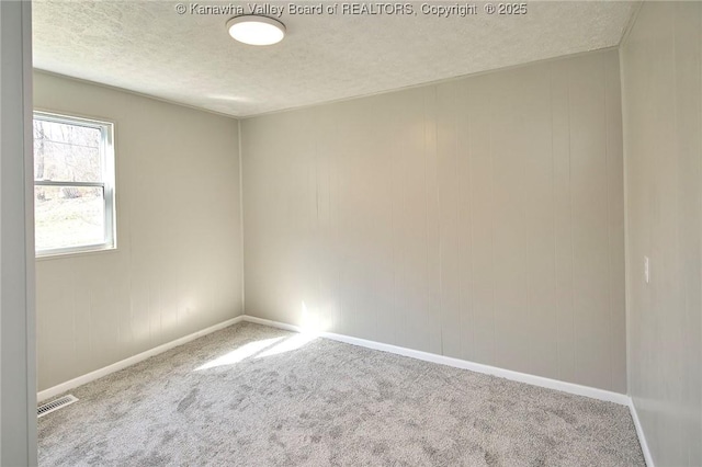 spare room featuring carpet flooring, baseboards, visible vents, and a textured ceiling