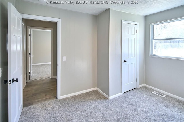 unfurnished bedroom featuring visible vents, a textured ceiling, a closet, carpet floors, and baseboards