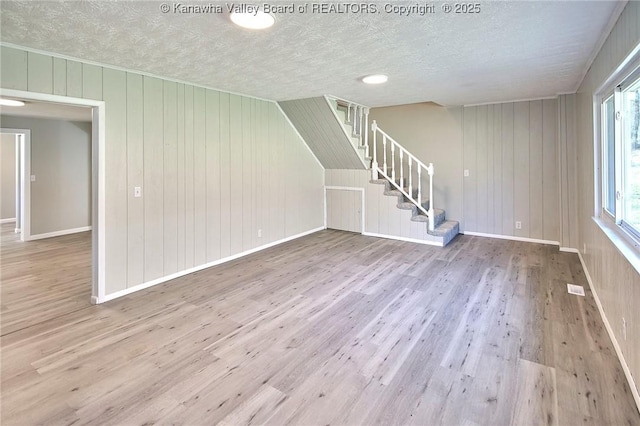 unfurnished living room featuring visible vents, baseboards, stairway, wood finished floors, and a textured ceiling