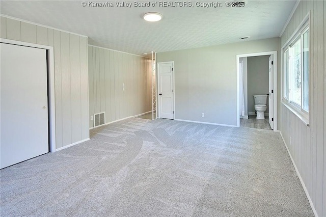 unfurnished bedroom featuring carpet, visible vents, baseboards, ornamental molding, and ensuite bathroom