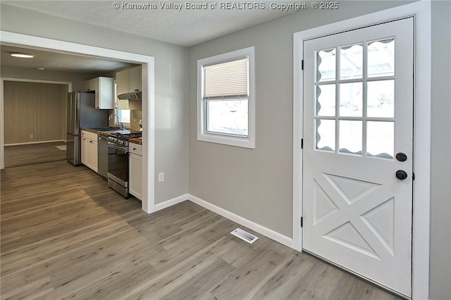 doorway to outside featuring visible vents, baseboards, light wood-type flooring, a textured ceiling, and a sink