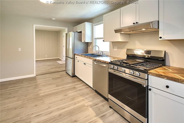 kitchen with under cabinet range hood, appliances with stainless steel finishes, light wood-style floors, white cabinetry, and a sink