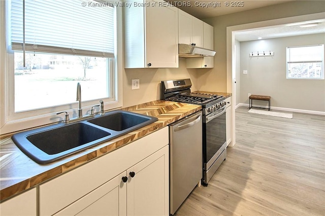 kitchen with under cabinet range hood, light wood-style flooring, appliances with stainless steel finishes, white cabinetry, and a sink