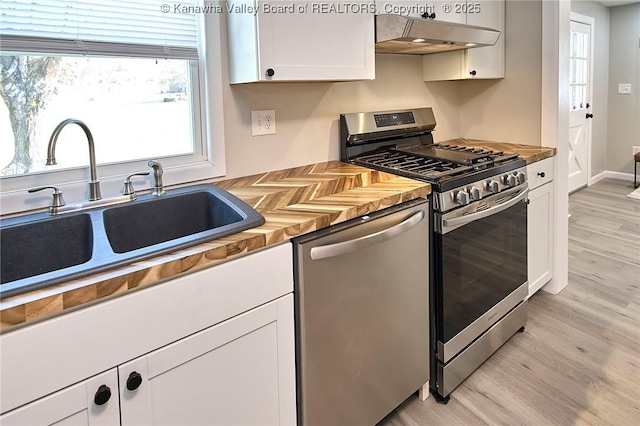 kitchen with light wood-style flooring, a sink, butcher block countertops, under cabinet range hood, and appliances with stainless steel finishes